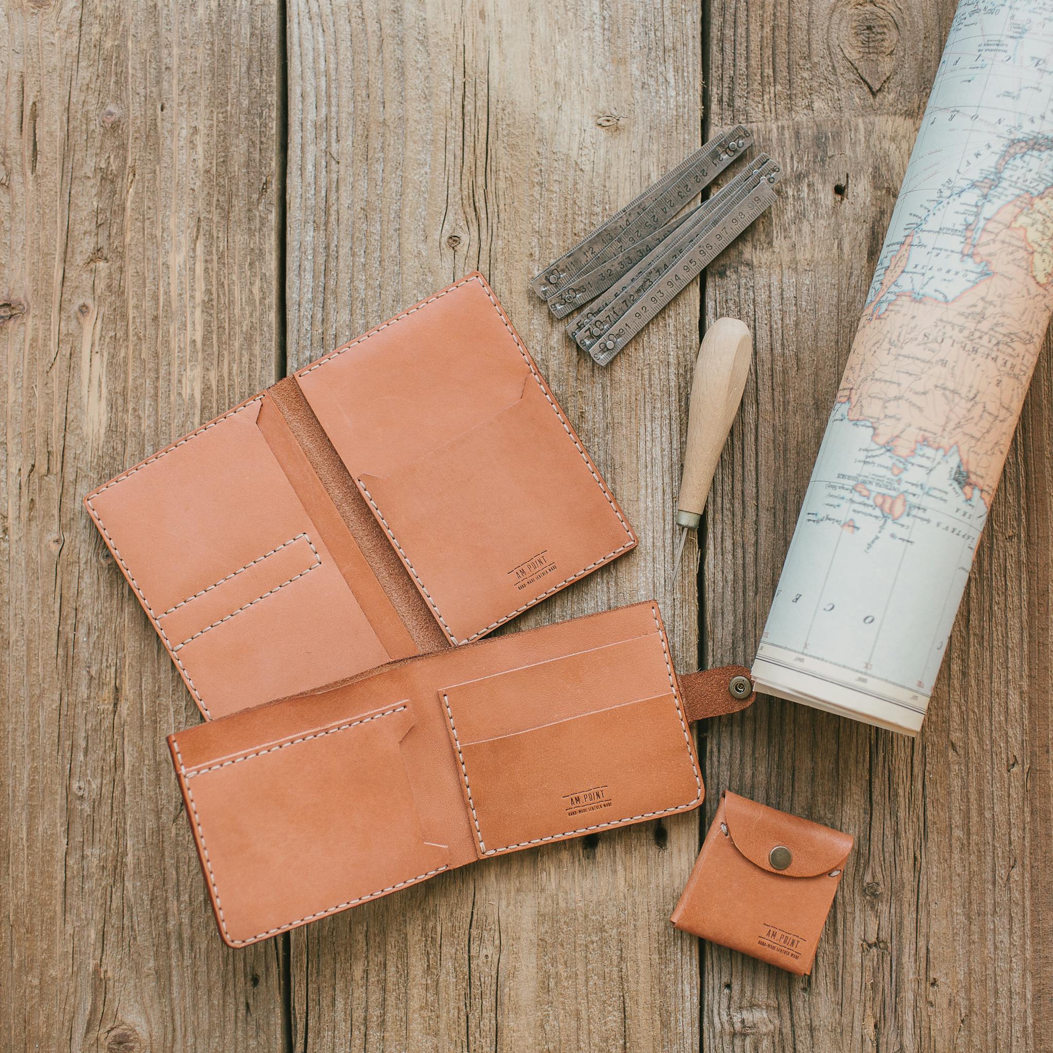 Flat lay of handmade leather wallet and tools on rustic wooden surface with a world map.